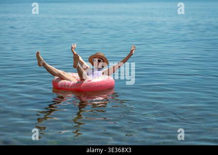 Woman, water, floating on pink donut inflatable ring in blue calm lake enjoying summer vacation. Stock Photo