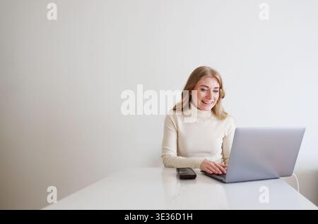 Happy female typing on laptop with phone nearby. Online business, remote work and technology concept. Stock Photo