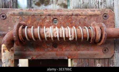 Close-up of an old, rusty metal sliding bolt latch with a spring mechanism mounted on a weathered wooden fence door Stock Photo