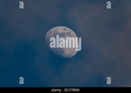 The moon photographed during the day against a blue sky with a partial crescent Stock Photo