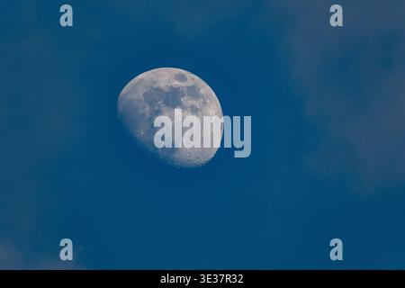 The moon photographed during the day against a blue sky with a partial crescent Stock Photo