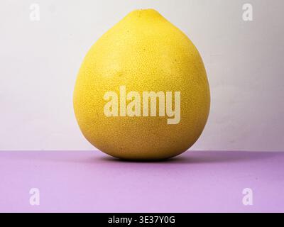 Yellow pomelo fruit sits on a purple surface with a light background Stock Photo