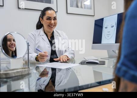 Smiling female doctor in white coat talking with a patient during a consultation in an aesthetic clinic, discussing potential cosmetic procedures and Stock Photo