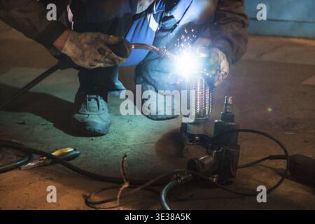Repairing of corrugation muffler of exhaust system in car workshop - mechanic welds the pipe on corrugation silencer by argon welding Stock Photo