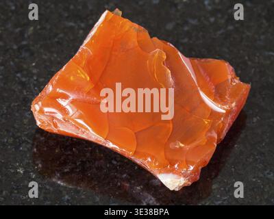 Macro shooting of natural mineral - rough fire opal gem stone on black granite from Ural Mountains Stock Photo