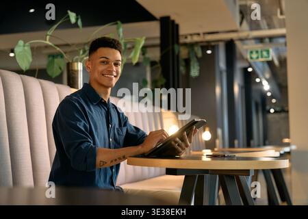 Happy young businessman smiling while using digital tablet in office lounge during evening Stock Photo