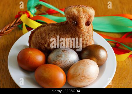 Small Easter lamb cake with painted eggs on white plate and traditional Czech pomlazka with colorful ribbons in background Stock Photo