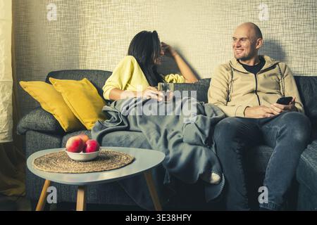 Young multi-ethnic couple laugh on cozy couch together, overjoyed laughing woman and man having fun, enjoying leisure time togetherness, relaxing in l Stock Photo