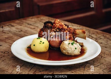 Munich, Germany - April 15, 2025: Traditional Bavarian pork knuckle served with dumplings and gravy inside the historic Hofbrauhaus beer hall in Munic Stock Photo
