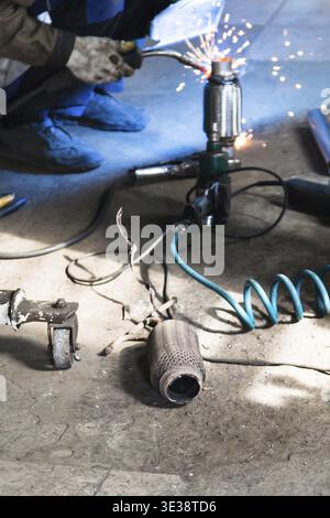 Repairing of corrugation muffler of exhaust system in car workshop - old burnt corrugation muffler on floor of workshop Stock Photo
