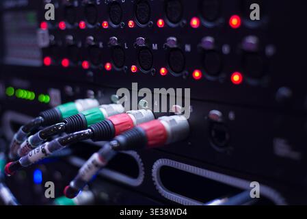 Close-up of XLR audio cables plugged into a professional patch panel with active signal indicator lights in a studio rack. High-quality sound routing Stock Photo