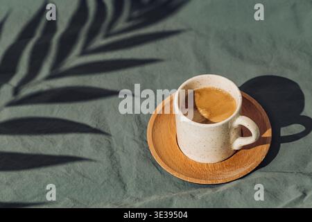 Summer day scene made with cup of coffee and tropical palm tree leaf shadow on linen background. Sun and shadows. Minimal summer coffee concept. Stock Photo