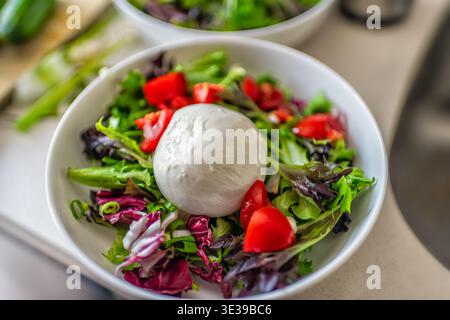 Burrata mozzarella Italian cheese on baby salad green spring mix tomatoes in white plate bowl macro closeup Stock Photo