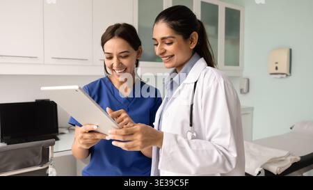 Two women doctors reviewing positive patient recovery updates on tablet Stock Photo