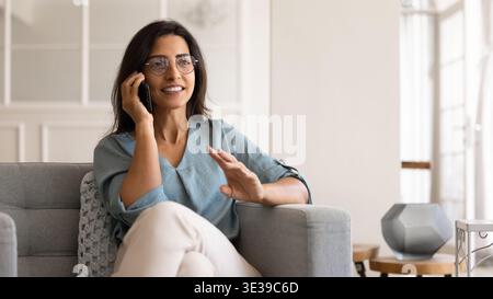 Woman sitting comfortable on couch, holding smartphone, lead conversation Stock Photo