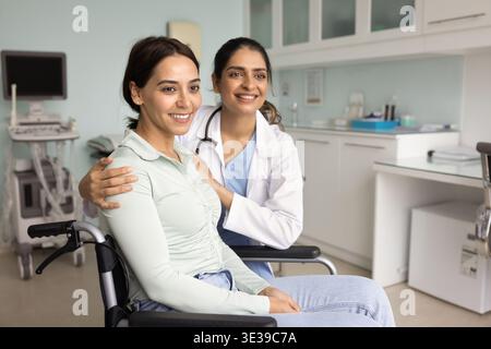 Female rehabilitation specialist embracing young woman patient in wheelchair Stock Photo