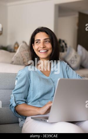 Smiling relaxed Brazilian woman using laptop on sofa Stock Photo