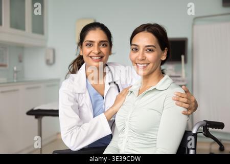 Young rehabilitation specialist hugging by shoulders patient sitting in wheelchair Stock Photo