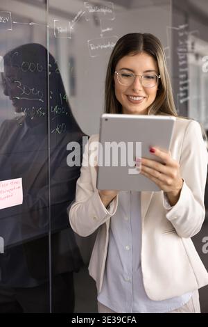 Professional businesswoman holding tablet standing near glass blackboard Stock Photo
