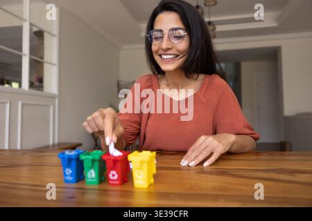 Woman placing piece of paper into miniature red recycling bin Stock Photo