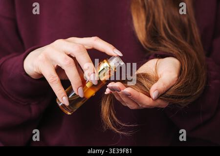Woman applying cosmetic oil to hair ends closeup. Haircare and beauty treatment routine with healthy long hair indoors at home. Stock Photo