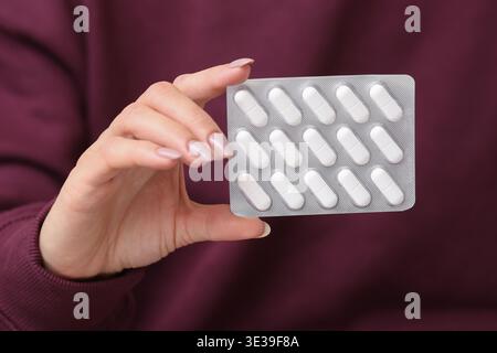 Hand holding blister pack with white pills. Medical tablets in foil packaging. Closeup of medication in female hand. Healthcare treatment concept. Stock Photo