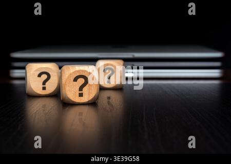 A close-up of wooden blocks with printed question marks on a dark polished desk. The central block and its reflection are in sharp focus. In the blurr Stock Photo
