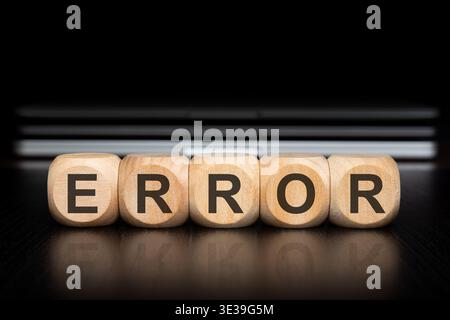 Close up of wooden toy blocks spelling the word ERROR with a clear reflection on a dark polished desk. In the blurred background, a stack of modern gr Stock Photo