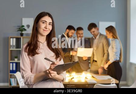 Portrait of smiling young businesswoman with professional team brainstorming on ideas in background. Stock Photo