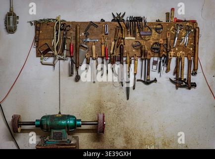 Specialty tools hang on a wooden board on the wall of a traditional artisanal craftsman leatherworks workshop in Florence, Italy Stock Photo