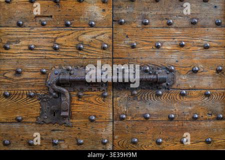 An ornate Renaissance metal latch and antique lock set mounted on thick, iron studded wooden door in the historic city of Florence, Tuscany, Italy Stock Photo