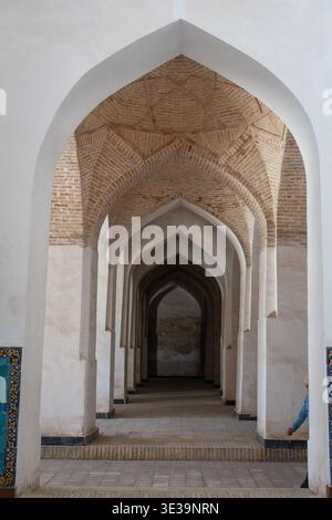Brick corridor with repeating pointed arches and intricate tilework, creating a deep geometric perspective under warm light Stock Photo