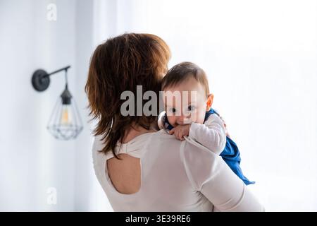Mother holding baby looking over shoulder at camera Stock Photo