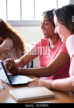 Cheerful female students sharing laptop in university Stock Photo
