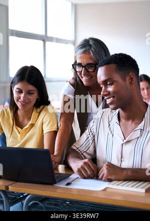 Teacher helping diverse students with laptop in classroom Stock Photo