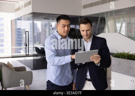 Asian businessman explaining project on tablet to colleague in office Stock Photo