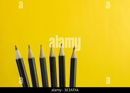 Close up of sharpened black pencils arranged in a row on bright yellow background, minimal creative concept with strong contrast and copy space. Stock Photo