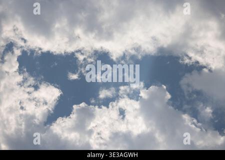 Soft white clouds drift across a bright blue sky. Sunlight breaks through gaps between the clouds. The sky feels calm and open. Perfect for background Stock Photo