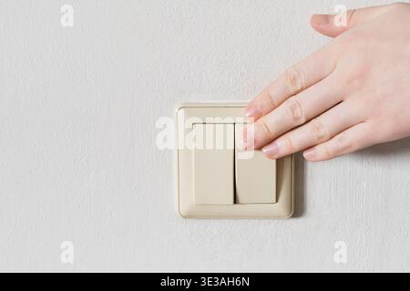 Hand turning off light switch on white wall, saving electricity Stock Photo