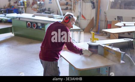 Senior worker sanding wood board in carpentry workshop Stock Photo