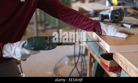 Carpenter drilling wood plank in a workshop Stock Photo