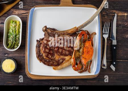 Grilled tomahawk steak with lobster tail served on wooden board Stock Photo