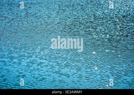 Blue water surface with small ripples and sparkling sunlight reflections creating abstract natural texture. Detailed pattern of lake water useful as b Stock Photo