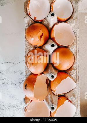 Top view of cracked brown eggshells arranged in a paper carton on a light marble surface. Minimalist kitchen still life symbolizing cooking, waste, re Stock Photo