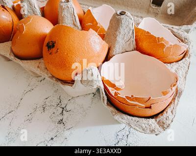 Close-up of cracked brown eggshells resting in a recycled paper carton on a light marble background. Natural kitchen still life illustrating cooking p Stock Photo
