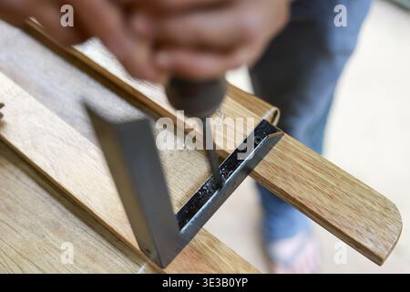 Close up of focused woodworker using screwdriver and try square for precision. person assembling wooden frame with metal bracket in home improvement p Stock Photo