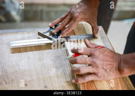 Close up of focused carpenter measuring wood with combination square. skilled craftsman hands show concentration and expertise while working on projec Stock Photo