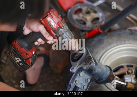 Focused mechanic hand uses cordless power tool for car suspension repair in an automotive garage. Close up detail on maintenance and assembly work Stock Photo