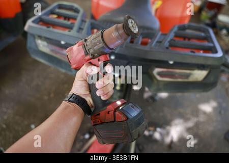 Close up of worker hand holding red cordless power tool in garage. Focused hands on manual labor for DIY repair project with rotary grinder attachment Stock Photo