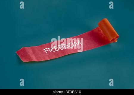 A scarlet band displaying the word freedom unrolls dynamically on a tranquil blue background, conveying a sense of release and new beginnings. Stock Photo